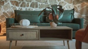Un salon moderne avec un mur en pierre, un canapé vert, une table basse en bois surmontée d’un panier tressé et un vase avec une plante.