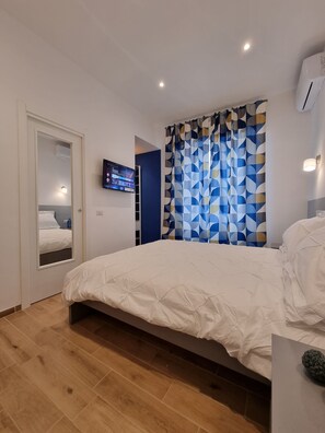 A bedroom with a bed, a TV mounted on the wall, and a patterned curtain. - G & G NAPOLI (Naples)