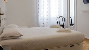 A bedroom with a bed, bedside tables, a chair, a TV mounted on the wall, and a window with curtains. - G & G NAPOLI (Naples)