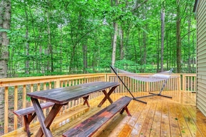 Relax on the deck surrounded by a dense forest, featuring a picnic table, benches, and a hammock.