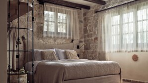 A bedroom with a stone wall, a bed with a beige blanket, a wicker basket, and a wooden headboard.