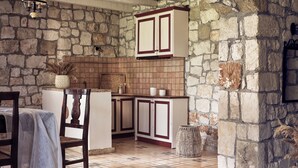 A rustic kitchen with stone walls, wooden cabinets, and a tiled floor.