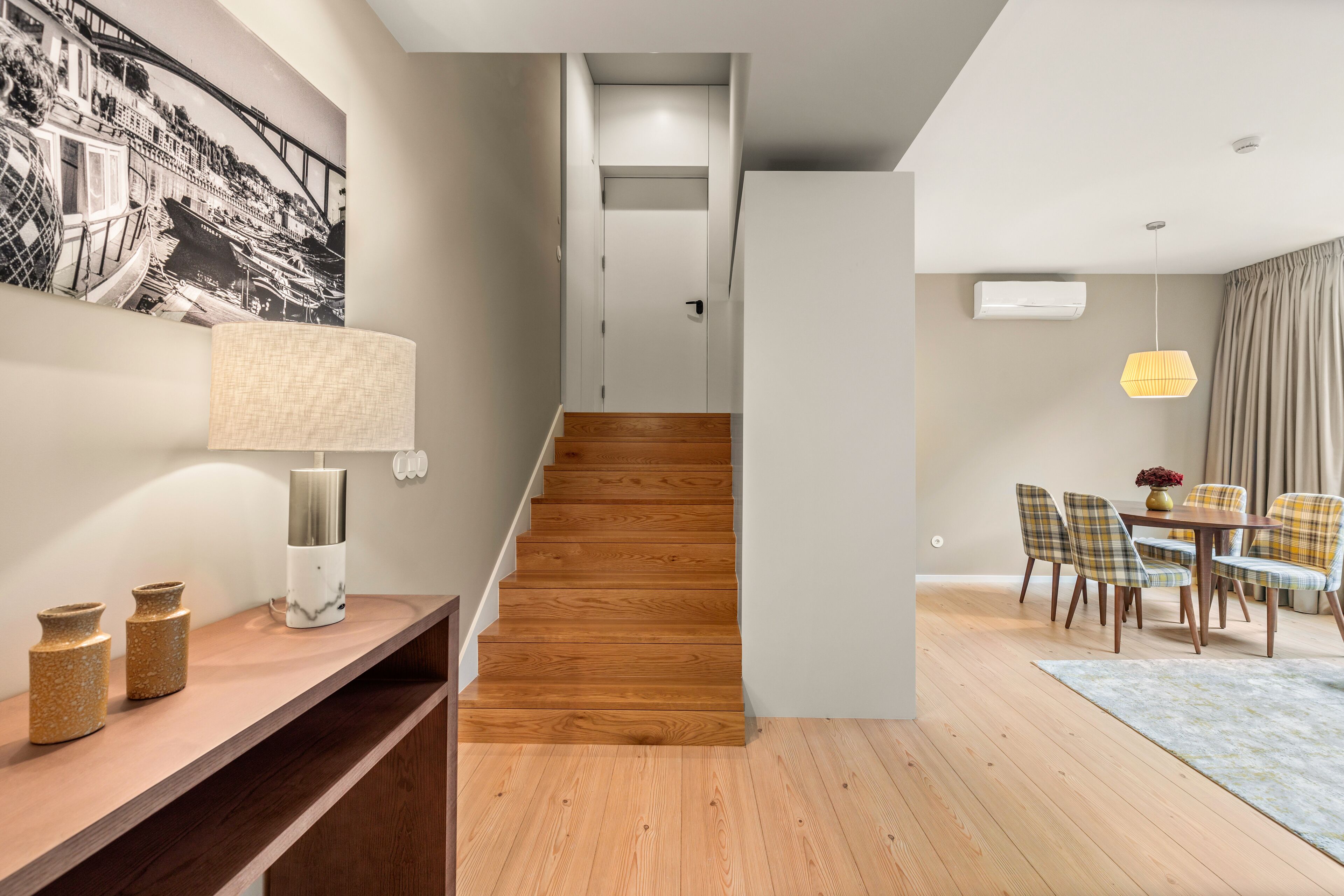 Ein modernes Interieur mit einer Holztreppe, einem Essbereich mit karierten Stühlen und einer wandmontierten Klimaanlage.
