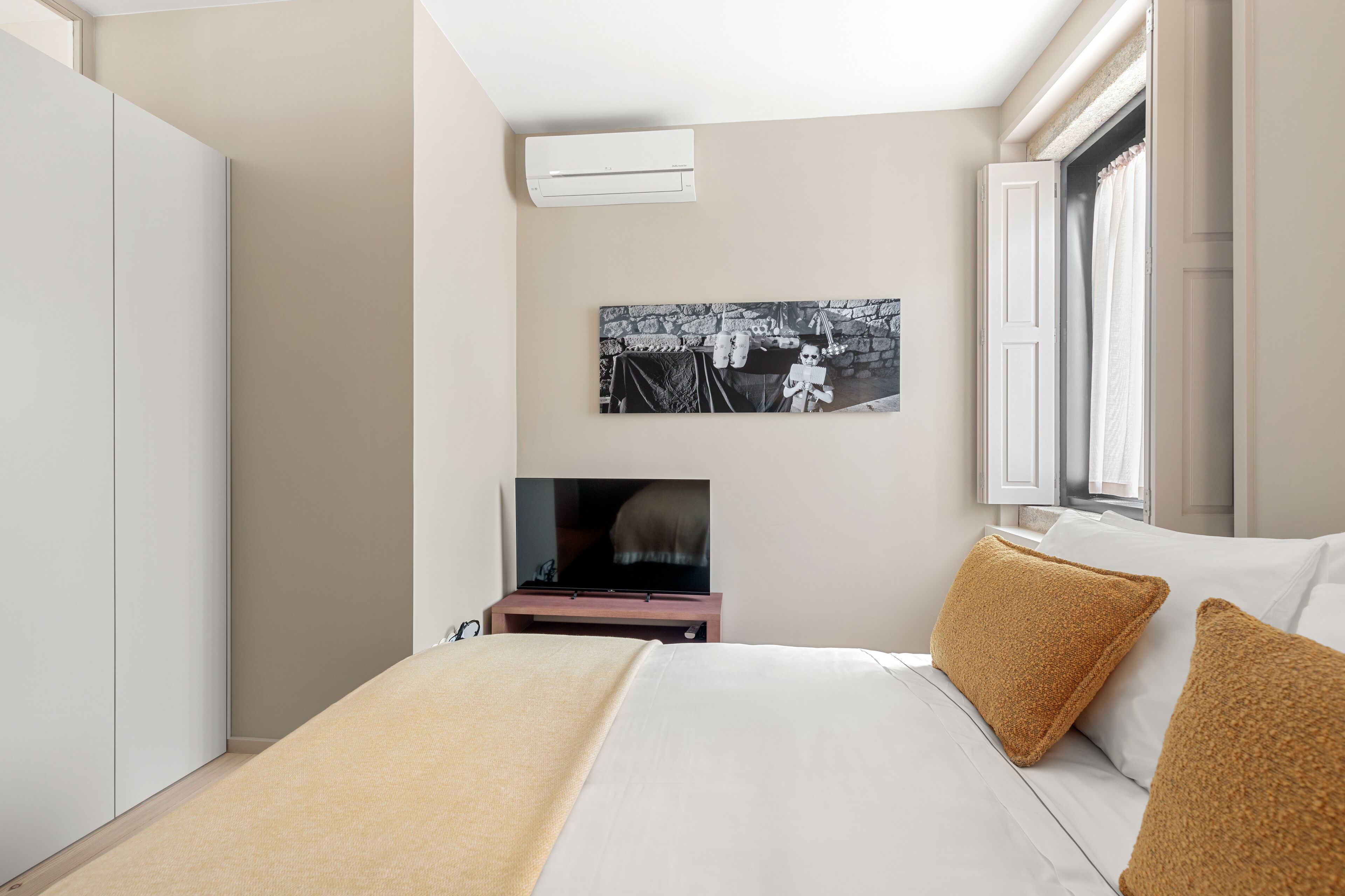A hotel room with a bed, a television, a wall-mounted picture, and a window with curtains.