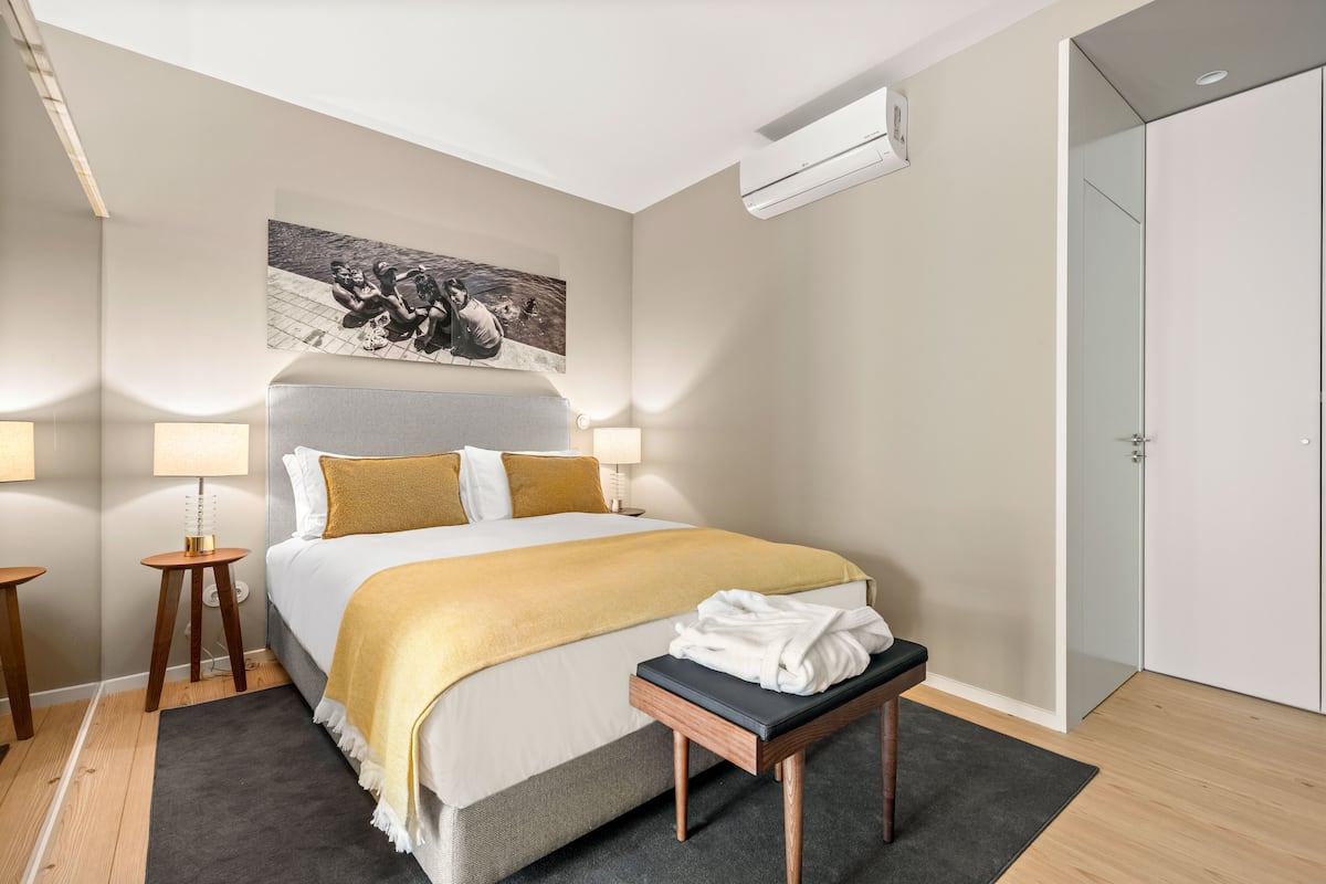 A neatly arranged hotel room with a large bed, a bedside table with a lamp, a bench with a towel, and a painting on the wall.