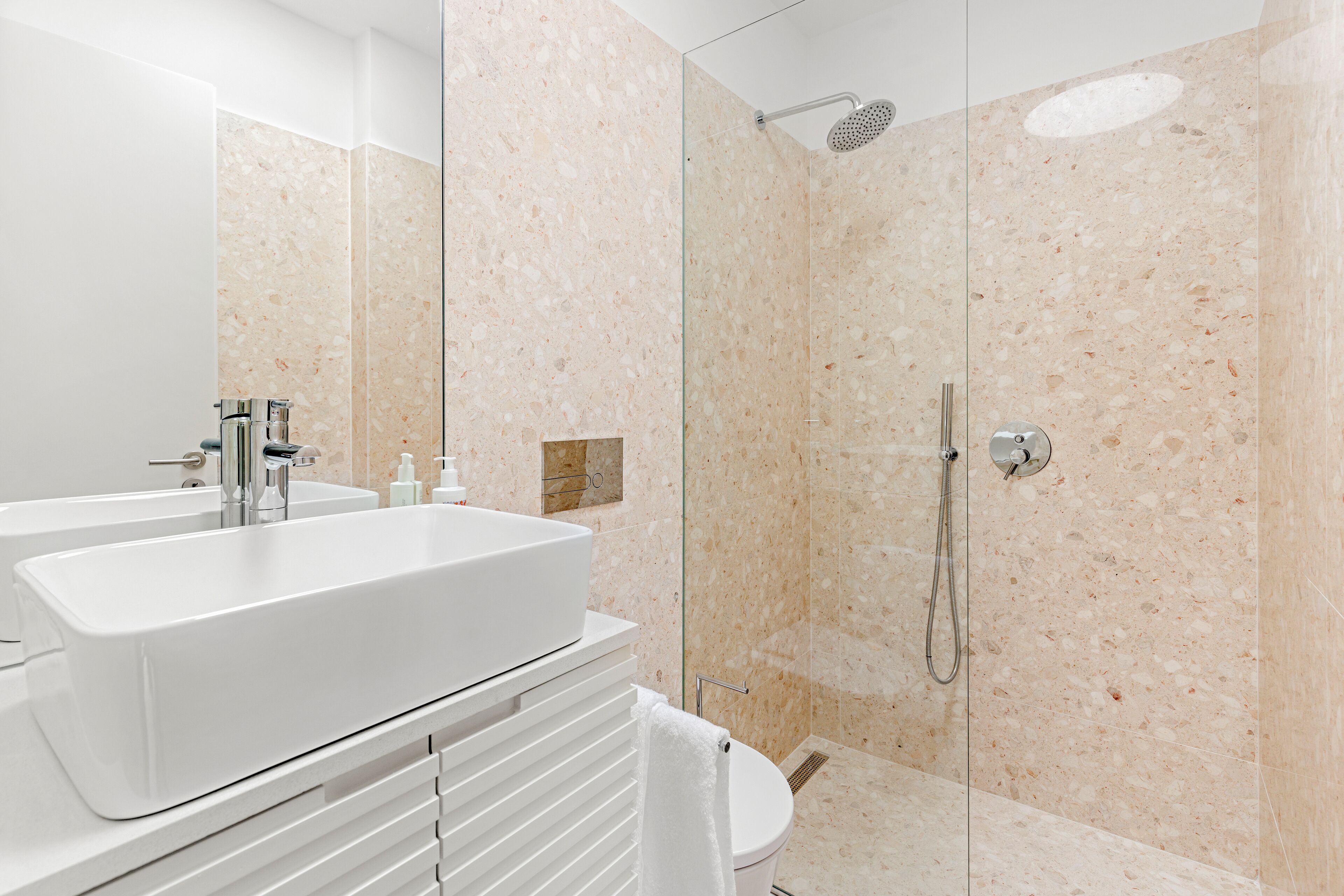 A modern bathroom with a large white sink, a glass-enclosed shower, and a toilet.