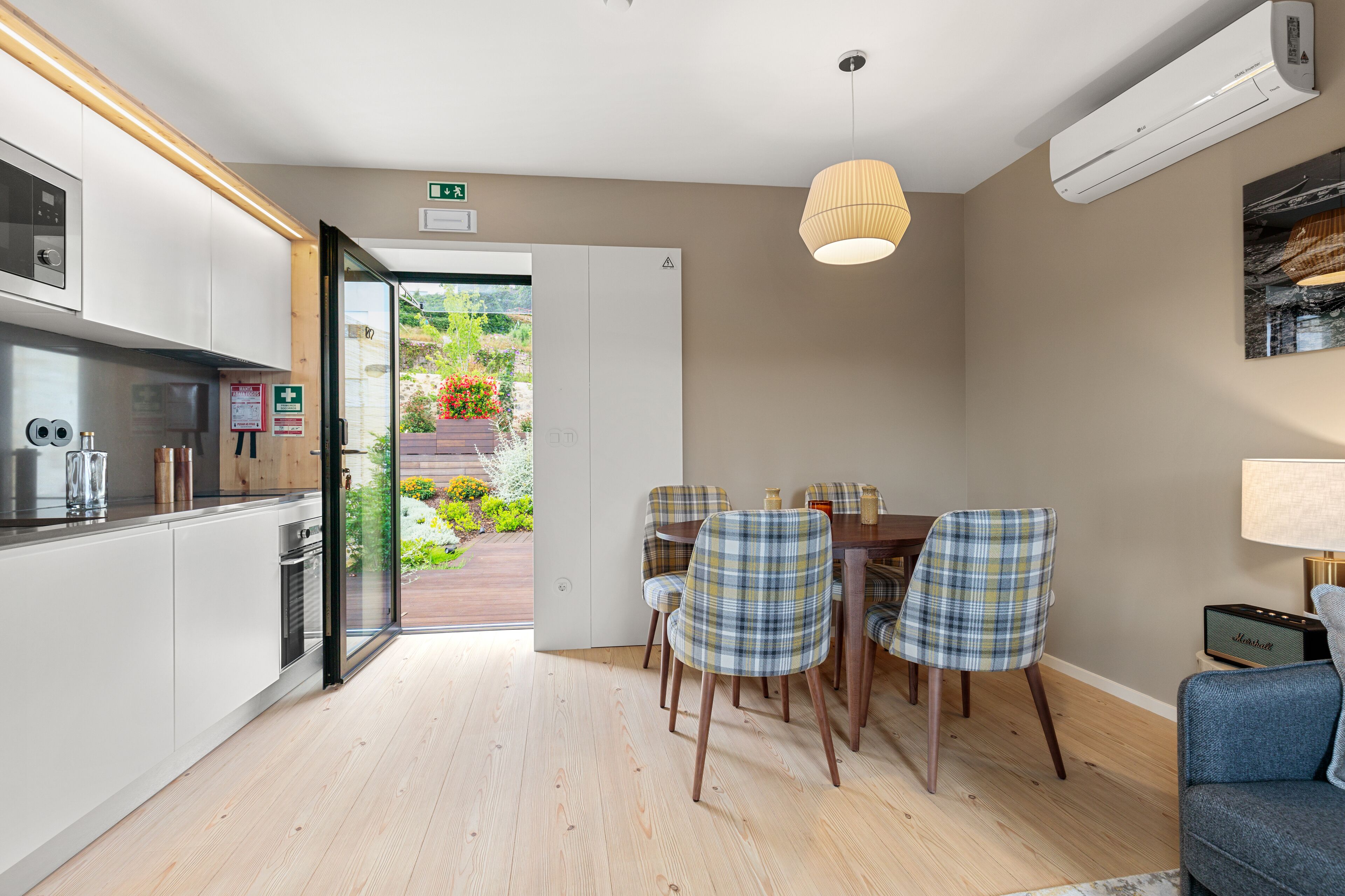 Una cocina moderna con comedor, piso de madera y vista a un jardín a través de una puerta abierta.