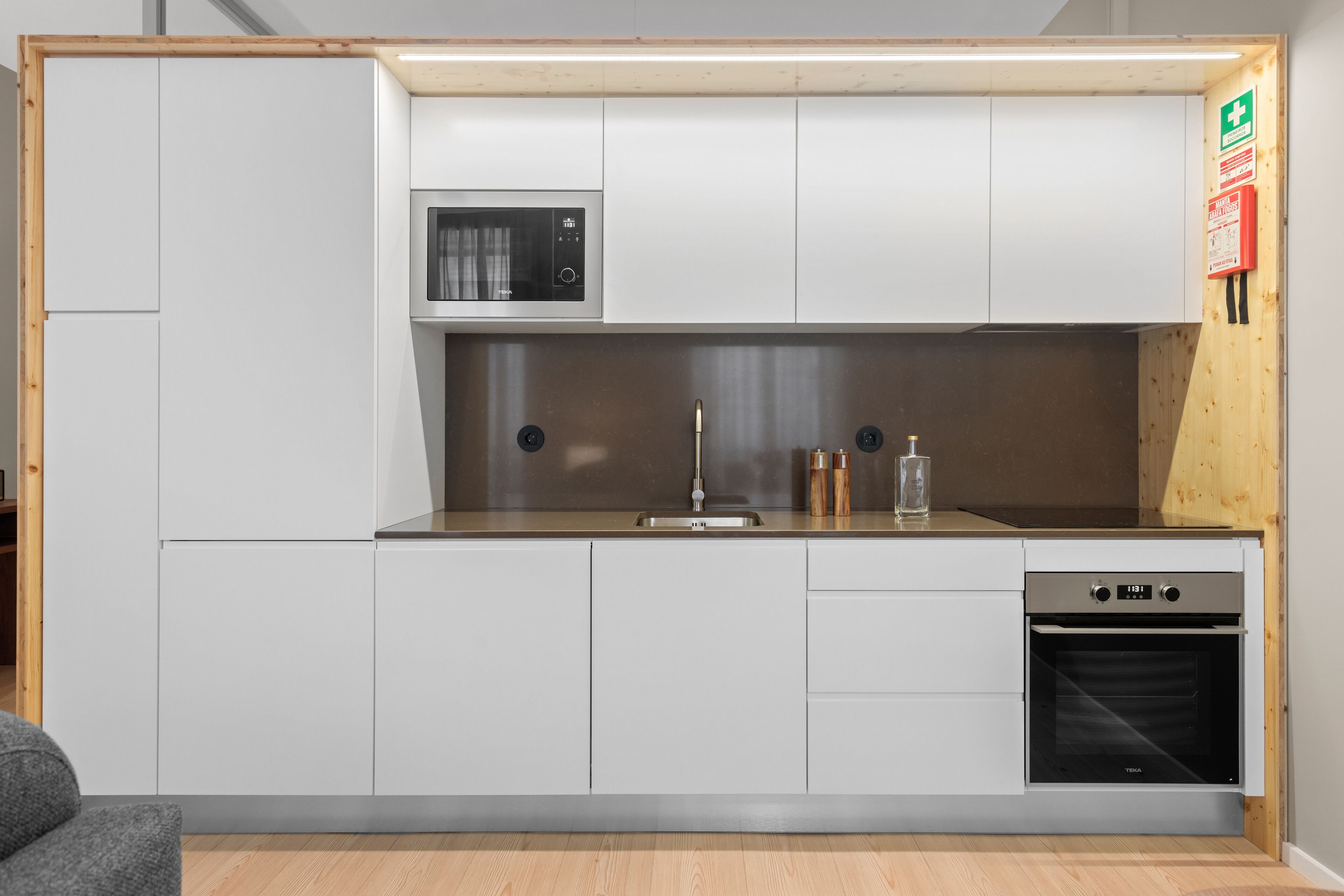 Una cocina compacta con armarios blancos, microondas, pileta, lavavajillas y horno integrado.