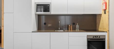 A compact kitchen with white cabinets, a microwave, a sink, a dishwasher, and a built-in oven.