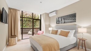 Une chambre à coucher moderne avec un grand lit, un téléviseur fixé au mur et une fenêtre avec des rideaux.