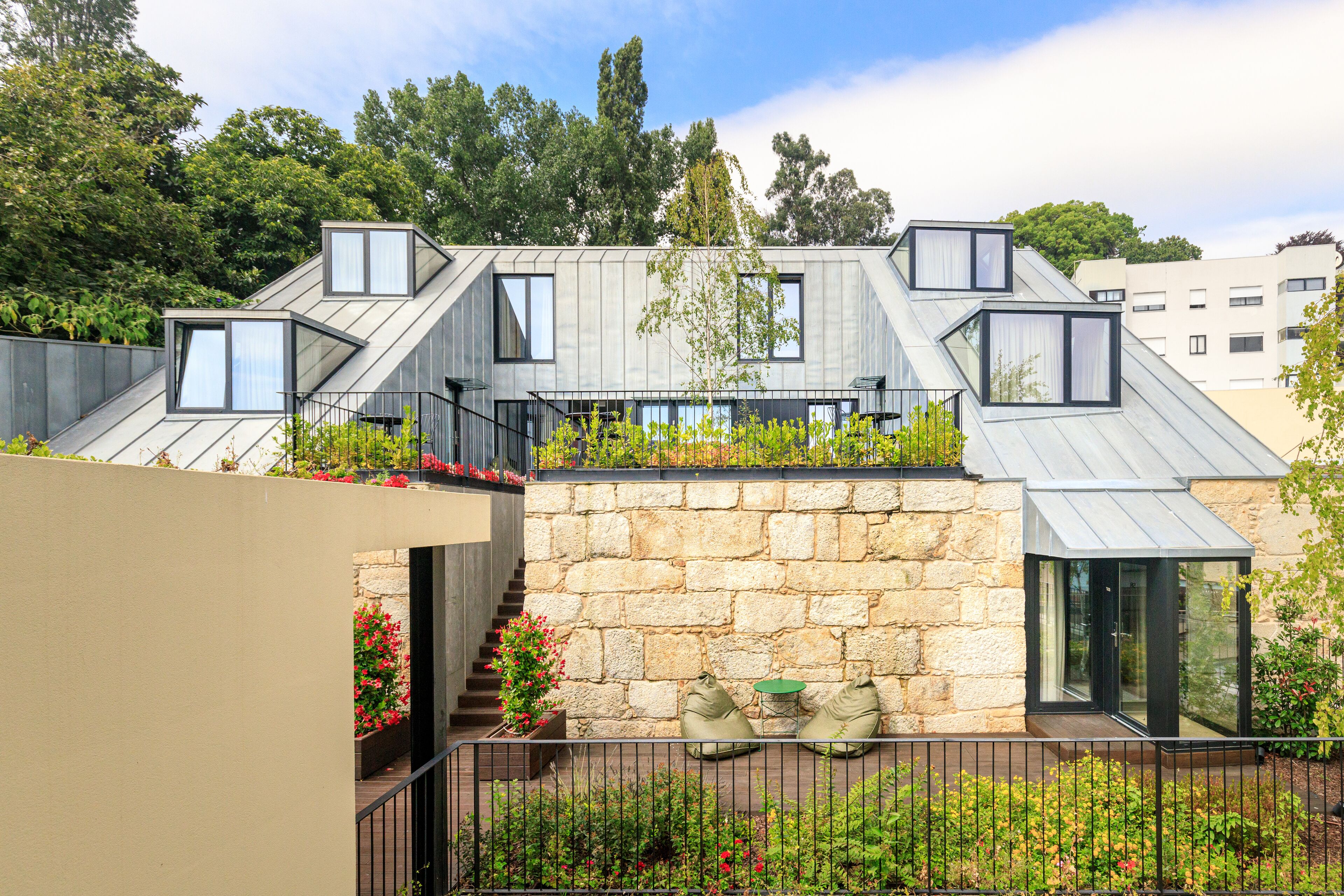 A modern house with a stone facade, a metal roof, and a small garden area with flowers and plants.