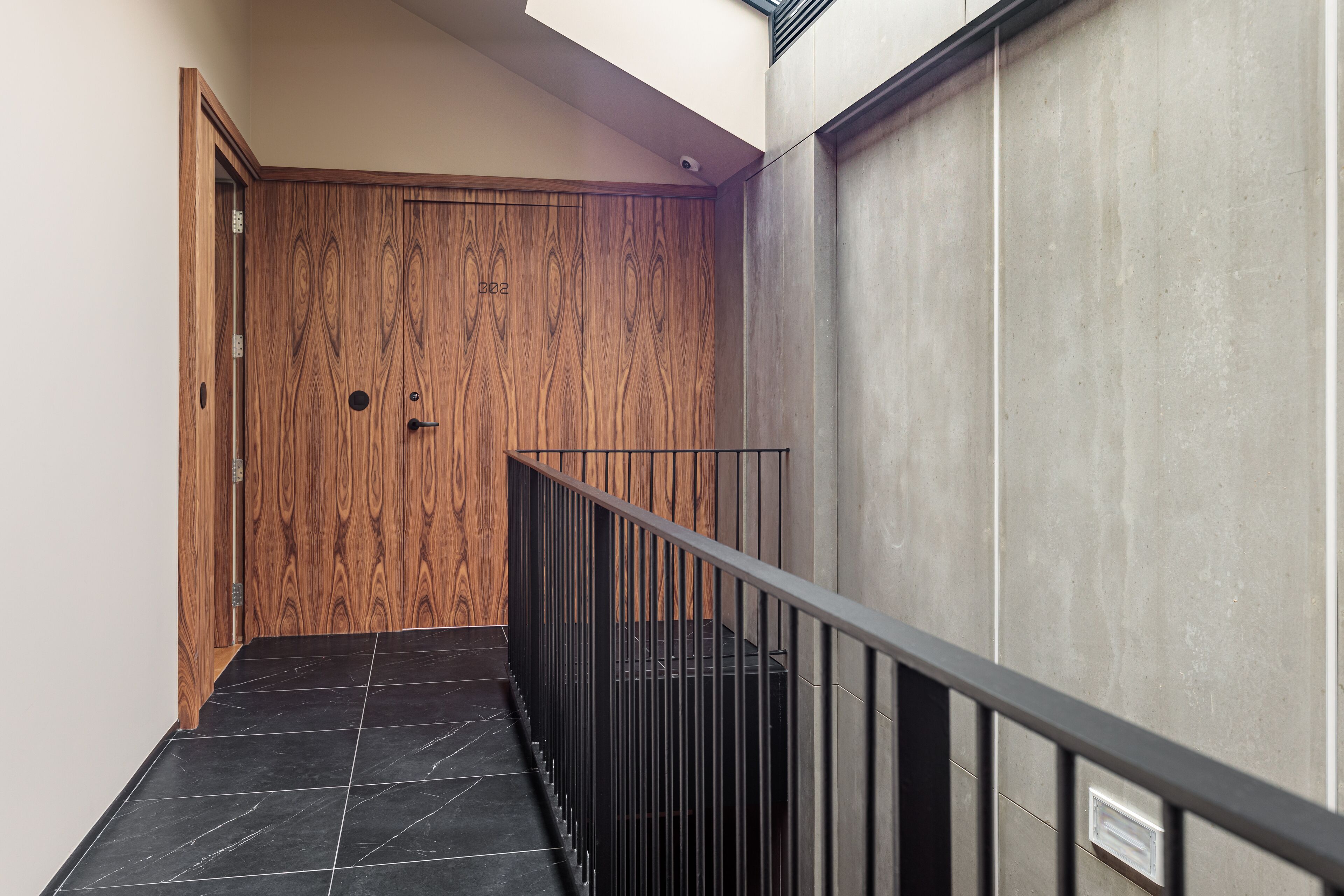 A modern interior with a wooden door, a concrete wall, and a metal railing.