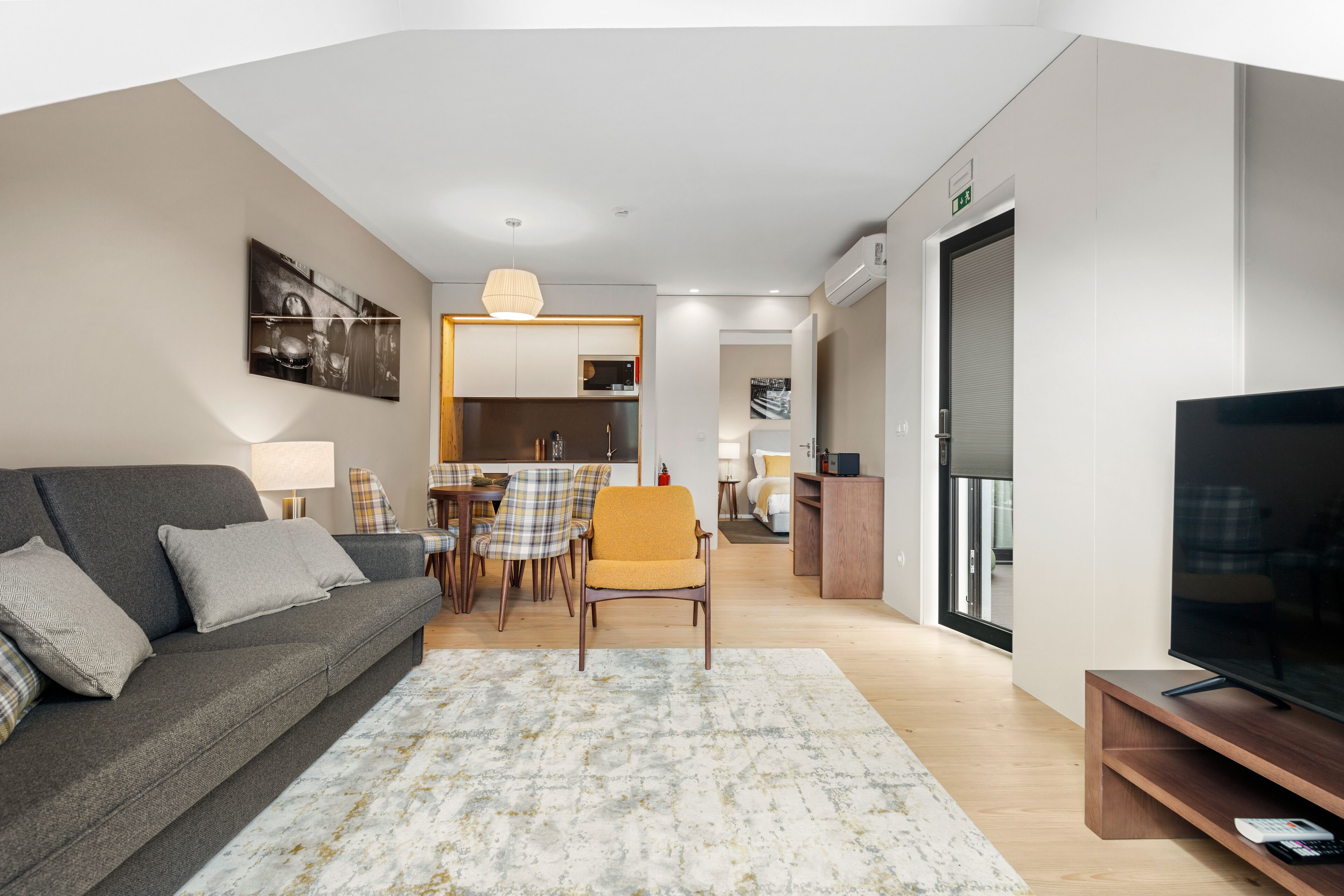 A modern living room with a sofa, a television, and a dining area with chairs and a table.