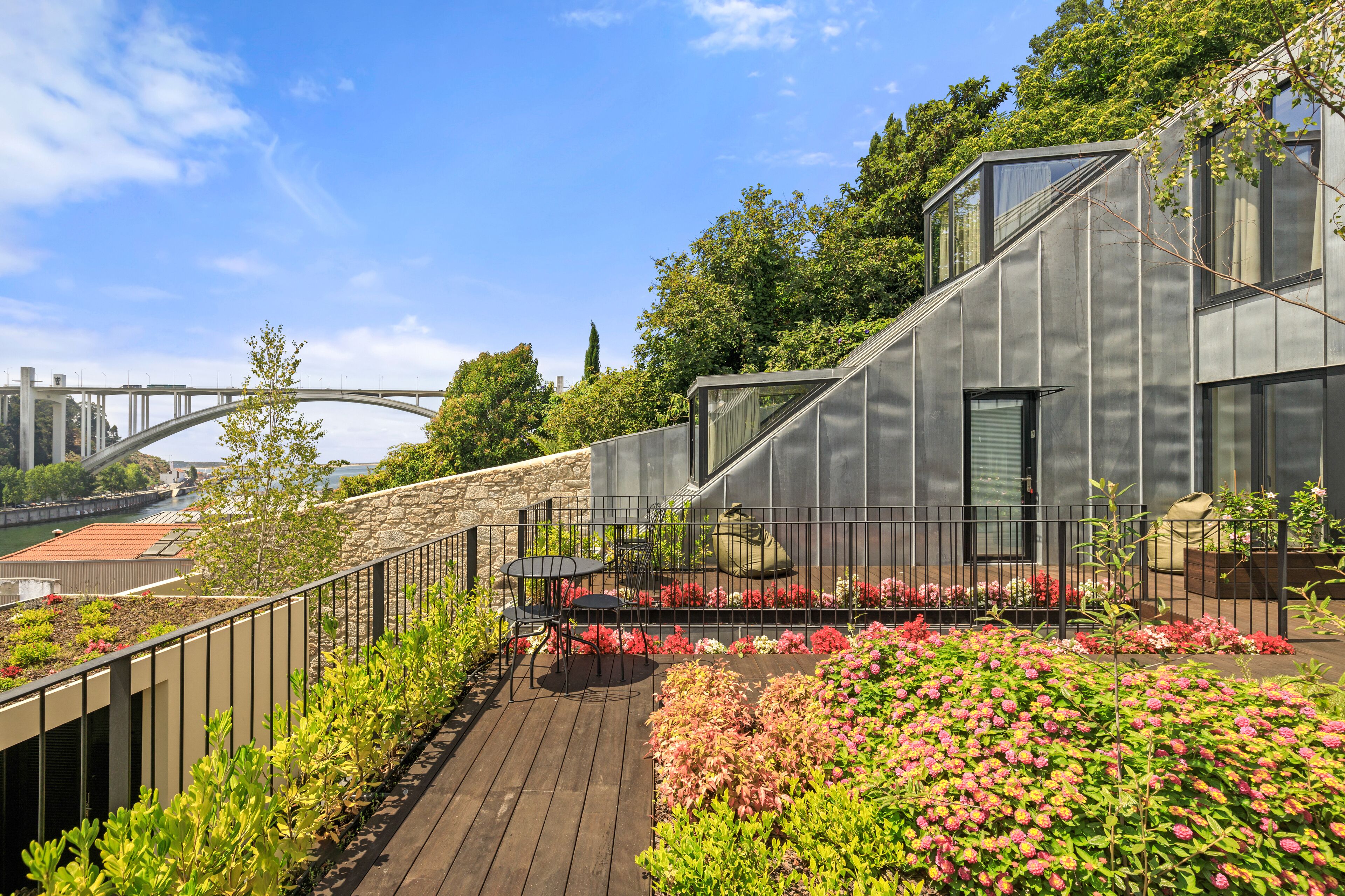 A rooftop garden with a wooden deck, metal railing, and potted plants.