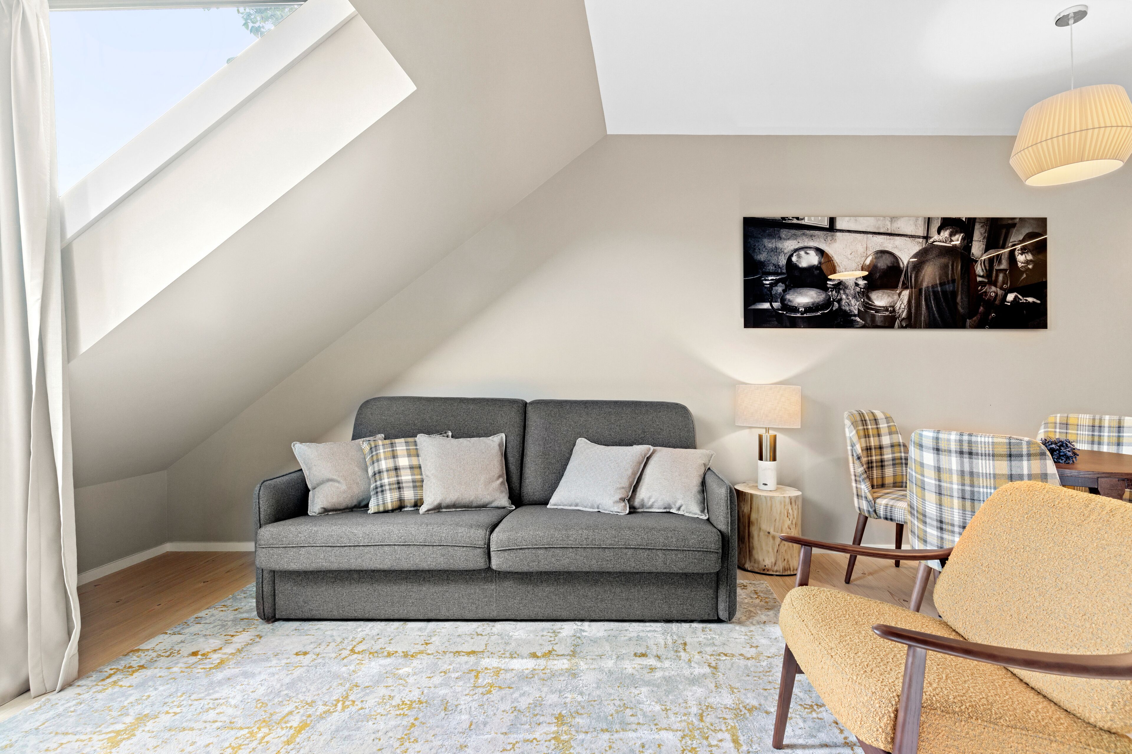Een moderne loft slaapkamer met een grijze bank, geruite fauteuils, een houten bijzettafeltje en een groot schilderij aan de muur.