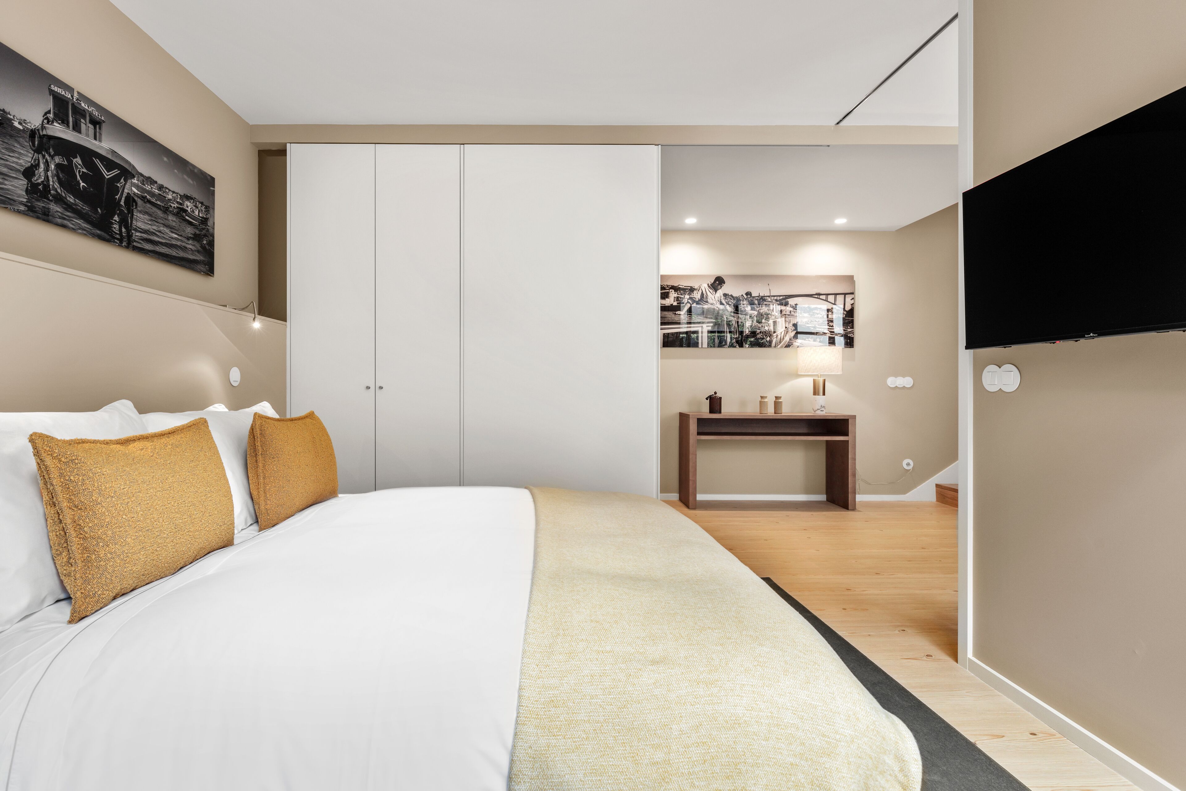 A modern hotel room with a large bed, a desk, a flat-screen TV, and artwork on the walls.