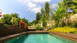 Une piscine aux eaux cristallines, bordée d’un mur de pierre et entourée de verdure.