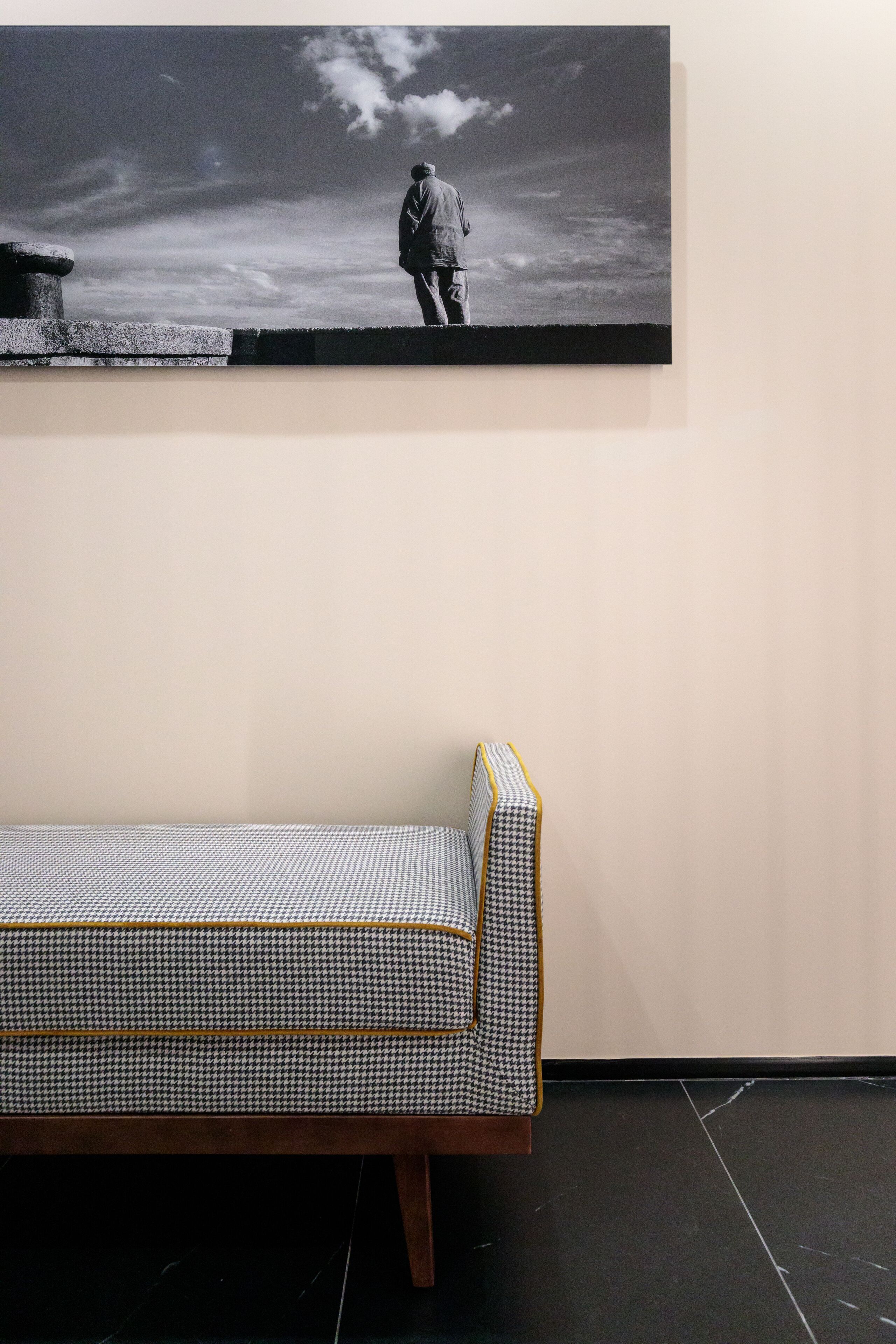 A room with a houndstooth-patterned sofa, a large framed artwork of a solitary figure, and a stone bench.