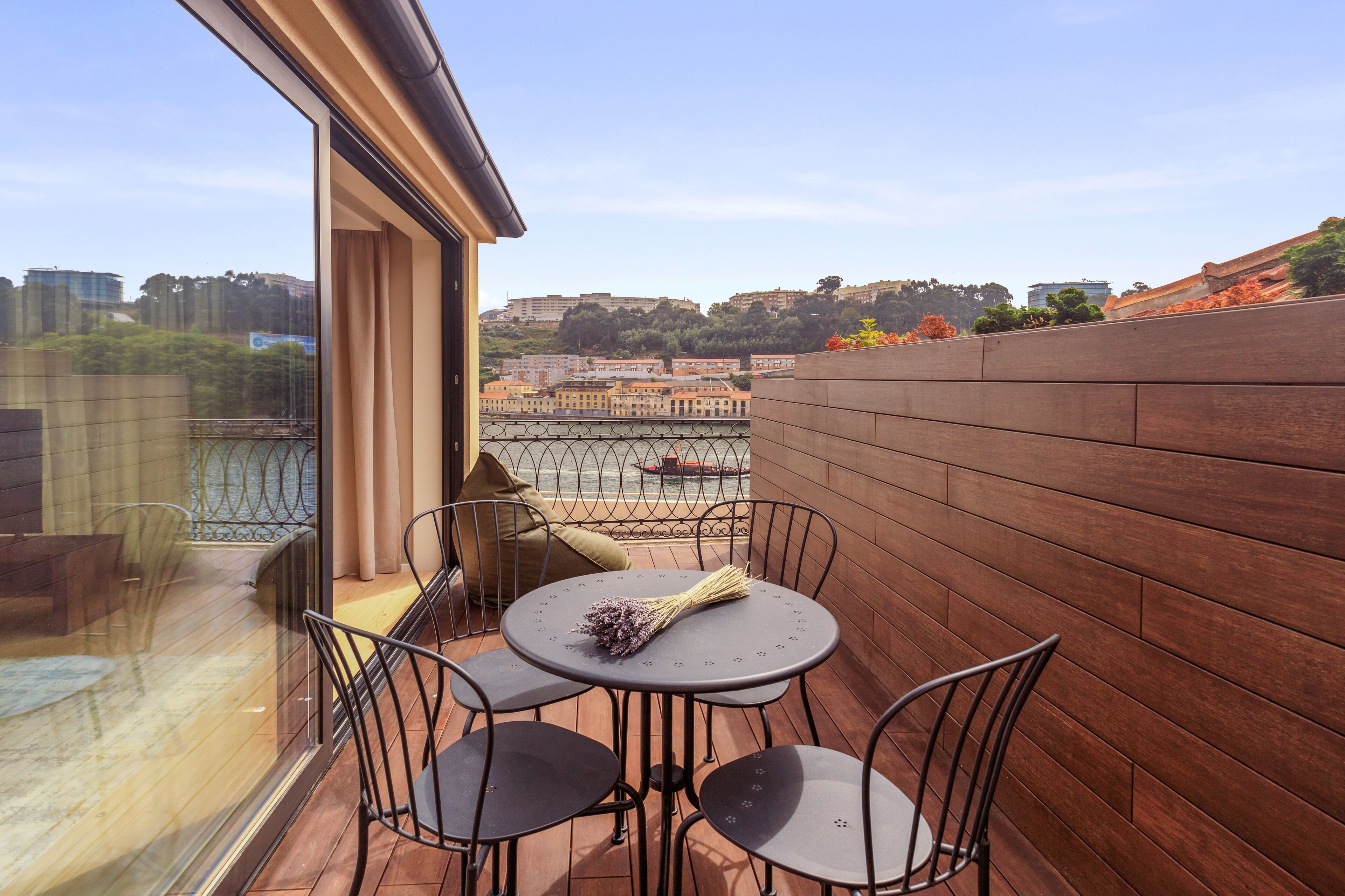 Ein Balkon mit rundem Tisch und vier Stühlen, Blick auf eine Stadtansicht und eine Holzwand.