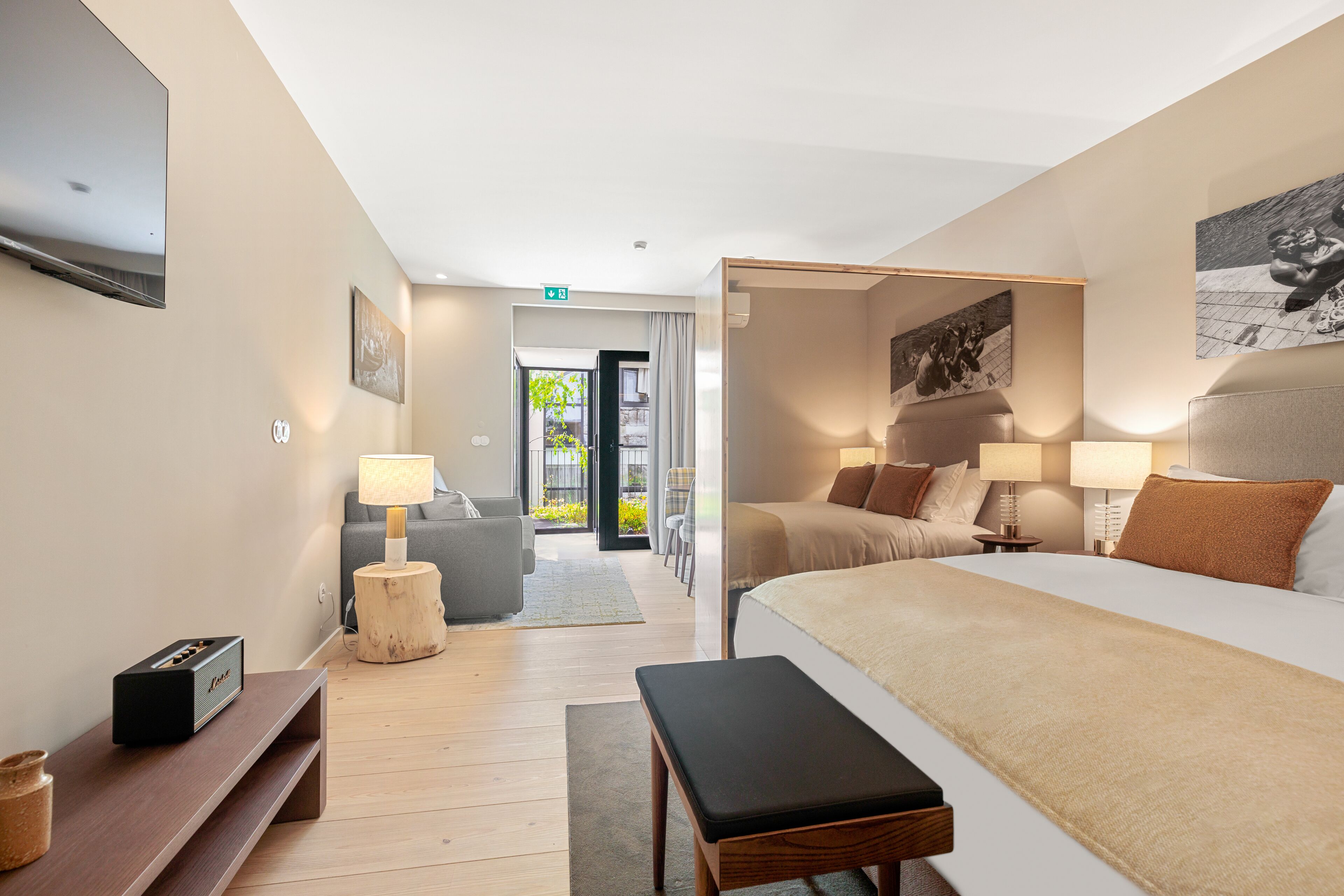 A modern hotel room with a large bed, bedside tables, a flat-screen TV, a sofa, and a view of the outdoors.