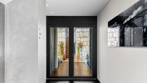 Un intérieur moderne avec une porte vitrée à cadre noir donnant sur une terrasse en bois agrémentée de fleurs rouges.