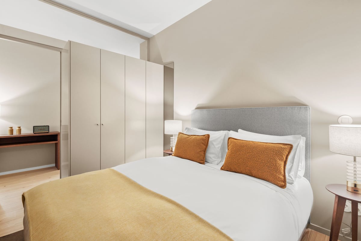 A hotel room with a bed, a bedside table, a lamp, and a wardrobe.