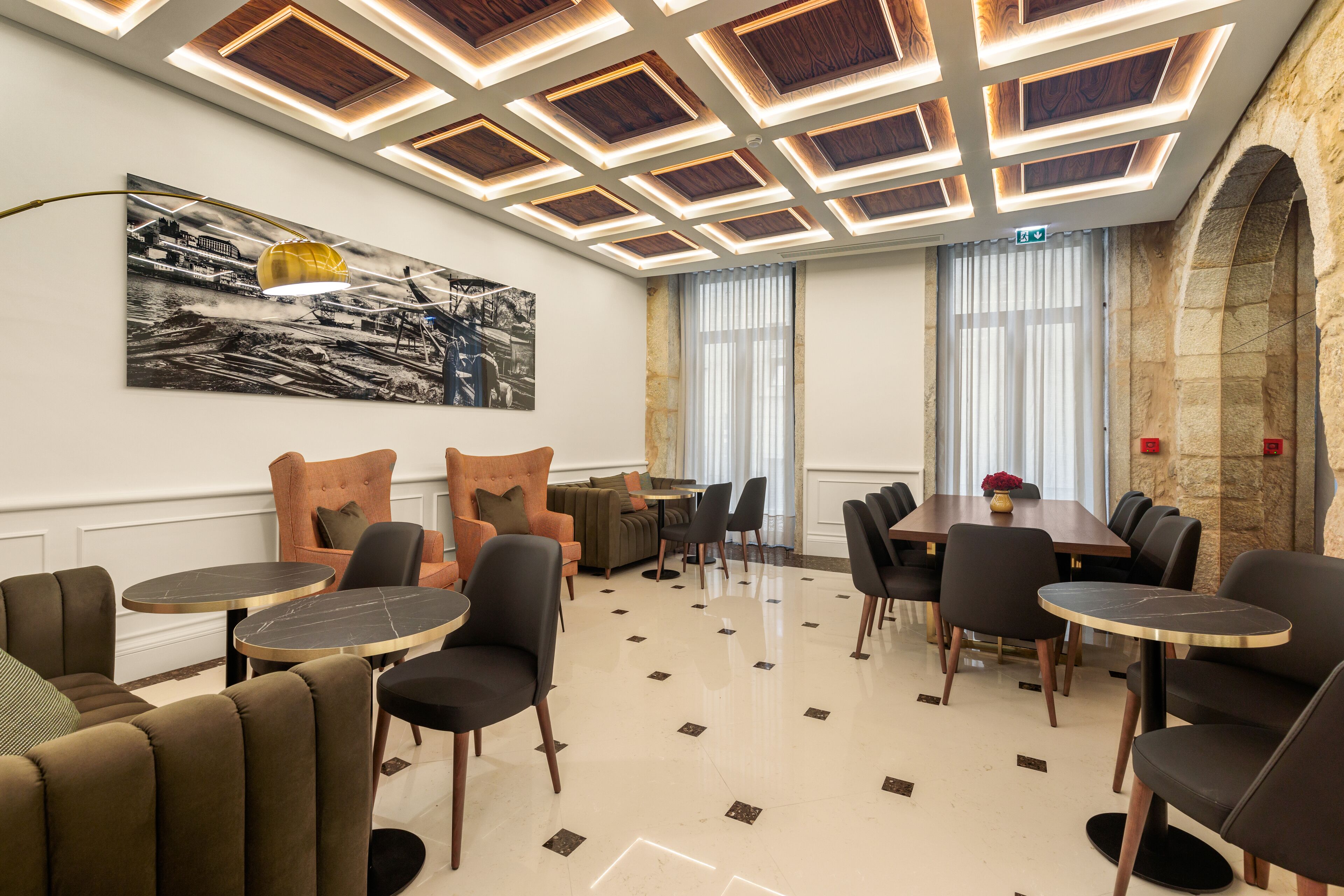 A modern dining area with a high ceiling, a large painting, and a stone wall.