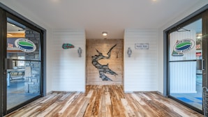Un piso de madera con un mosaico central en la pared, dos puertas con indicaciones y un logotipo en las paredes.