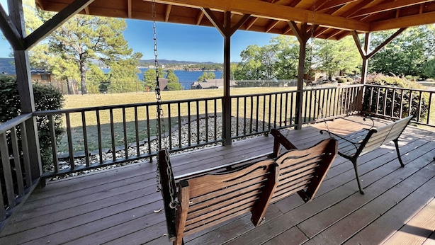 Una terraza techada con bancos de madera y una hamaca, con vista a un lago y árboles.