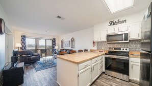 Una cocina moderna con armarios blancos, una isla grande, electrodomésticos de acero inoxidable y un comedor con vistas.