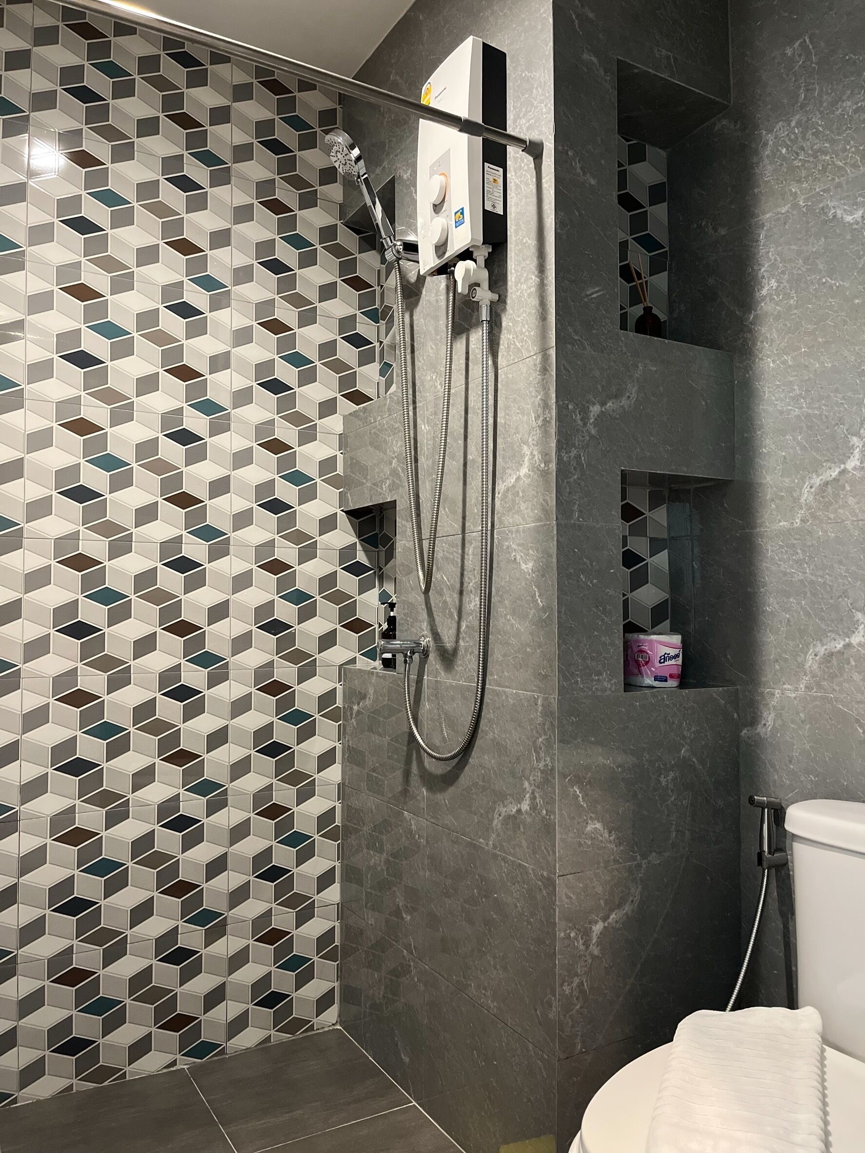 Un baño moderno con un salpicadero de azulejos geométricos, una ducha con cabezal de ducha manual y un inodoro.