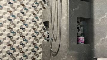 Un baño moderno con un salpicadero de azulejos geométricos, una ducha con cabezal de ducha manual y un inodoro.
