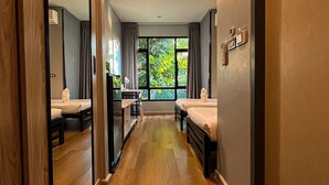 Un pasillo de hotel con piso de madera, un ventanal con cortinas y una cama a la derecha.