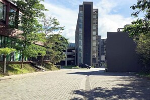 A modern building with a glass facade, surrounded by trees and a paved area.
