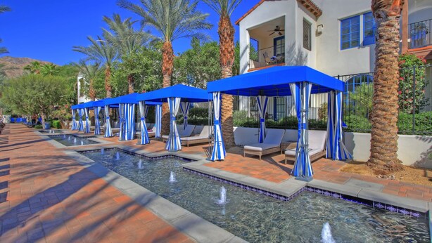 A pool area with blue canopies, lounge chairs, and palm trees. - LV111 One Bedroom Legacy Villa Near Main Pool (La Quinta)