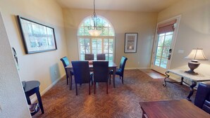 A dining area with a table, chairs, a chandelier, and a window with blinds. - LV111 One Bedroom Legacy Villa Near Main Pool (La Quinta)