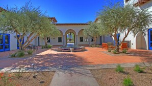 A courtyard with a fountain, outdoor seating, and a building with blue doors and arches. - LV111 One Bedroom Legacy Villa Near Main Pool (La Quinta)