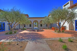 A courtyard with a fountain, outdoor seating, and a building with blue doors and arches.