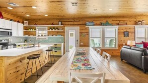 A cabin interior with a wooden ceiling, a kitchen with a bar area, a dining table with chairs, and a sofa. - Village Walk 3 BR/2.5 Bath--Shared Heated Pool and Close to the Beach! (Port Aransas)