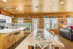 Cozy cabin kitchen with a central island, microwave, and sink, adjacent to a dining table with white chairs.