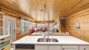 A cabin interior with a central island kitchen, wooden walls, and a cozy living area with a sofa and coffee table. - Village Walk 3 BR/2.5 Bath--Shared Heated Pool and Close to the Beach! (Port Aransas)
