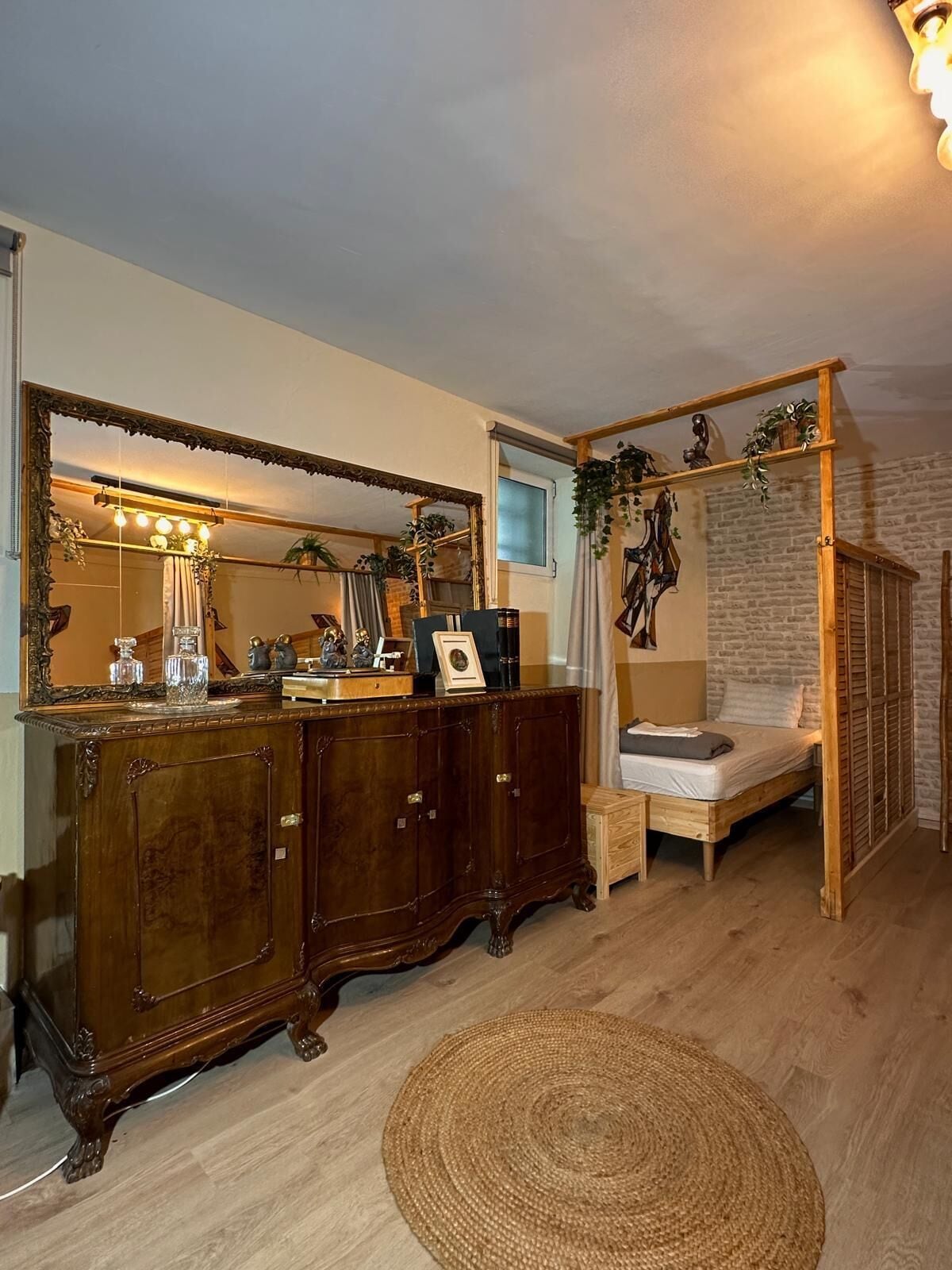 Una habitación con una cama de madera, un espejo grande, un aparador y un tapete redondo pequeño.