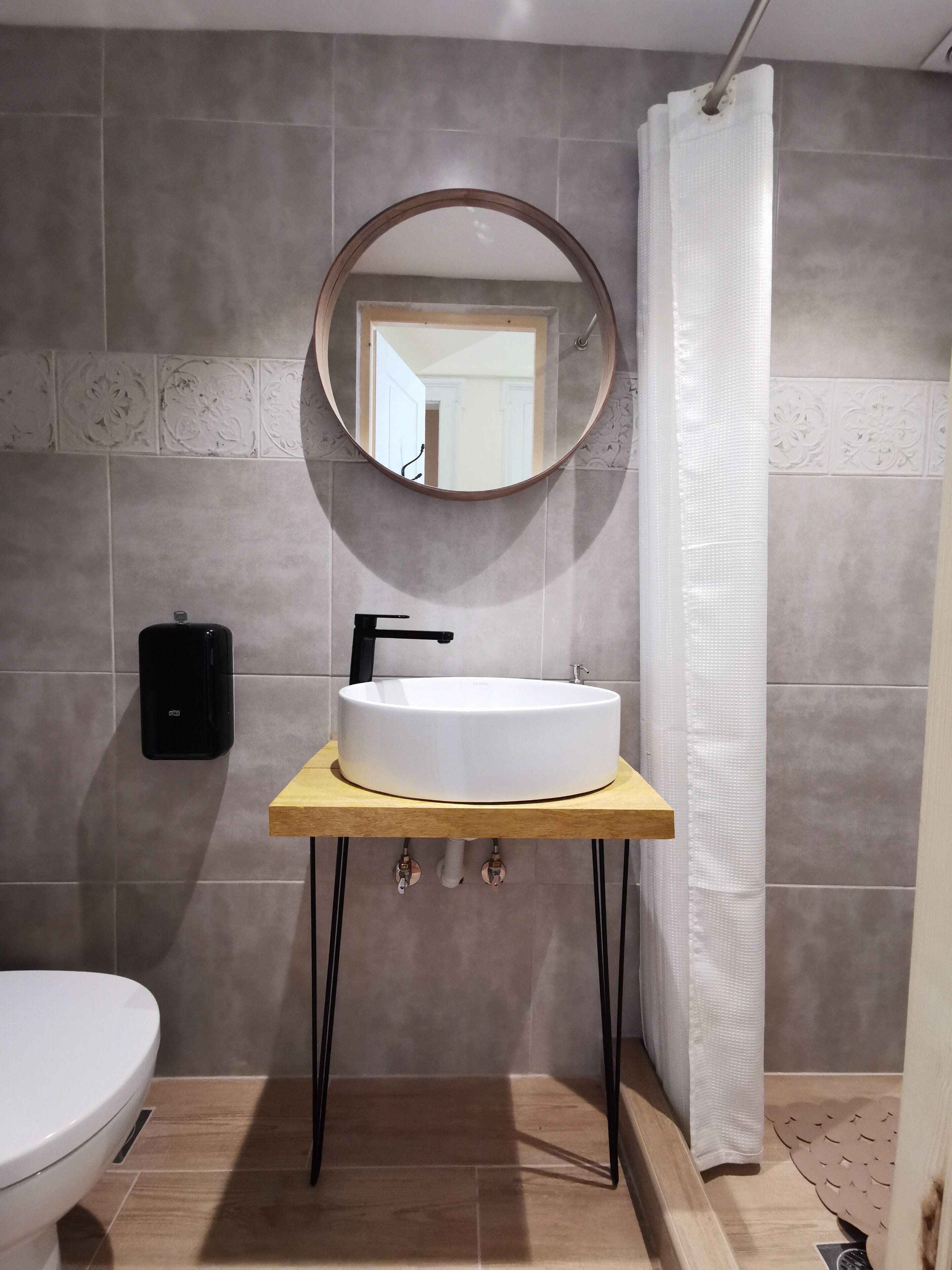 A bathroom with a round mirror, a white sink, and a toilet.