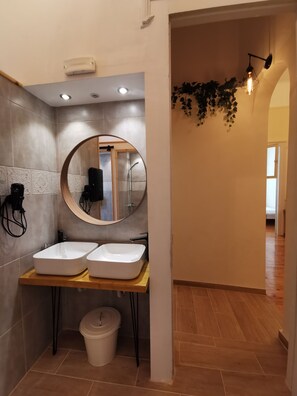 A modern bathroom with two white sinks, a round mirror, and a wooden vanity. - Baloo Hostel (Athens)