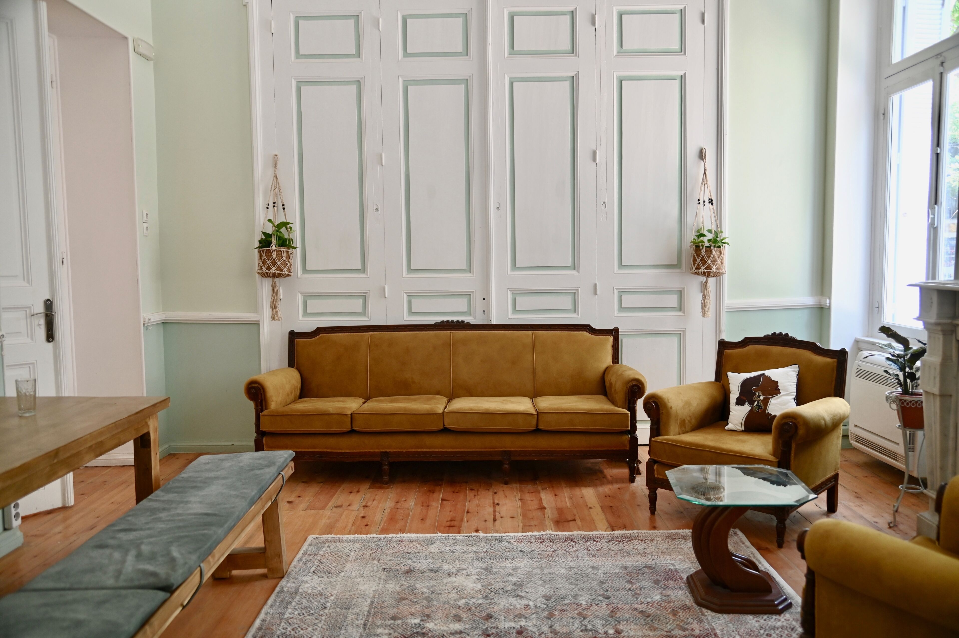Un salon avec un canapé marron, un banc en bois, une table basse en verre et un tapis à motifs.