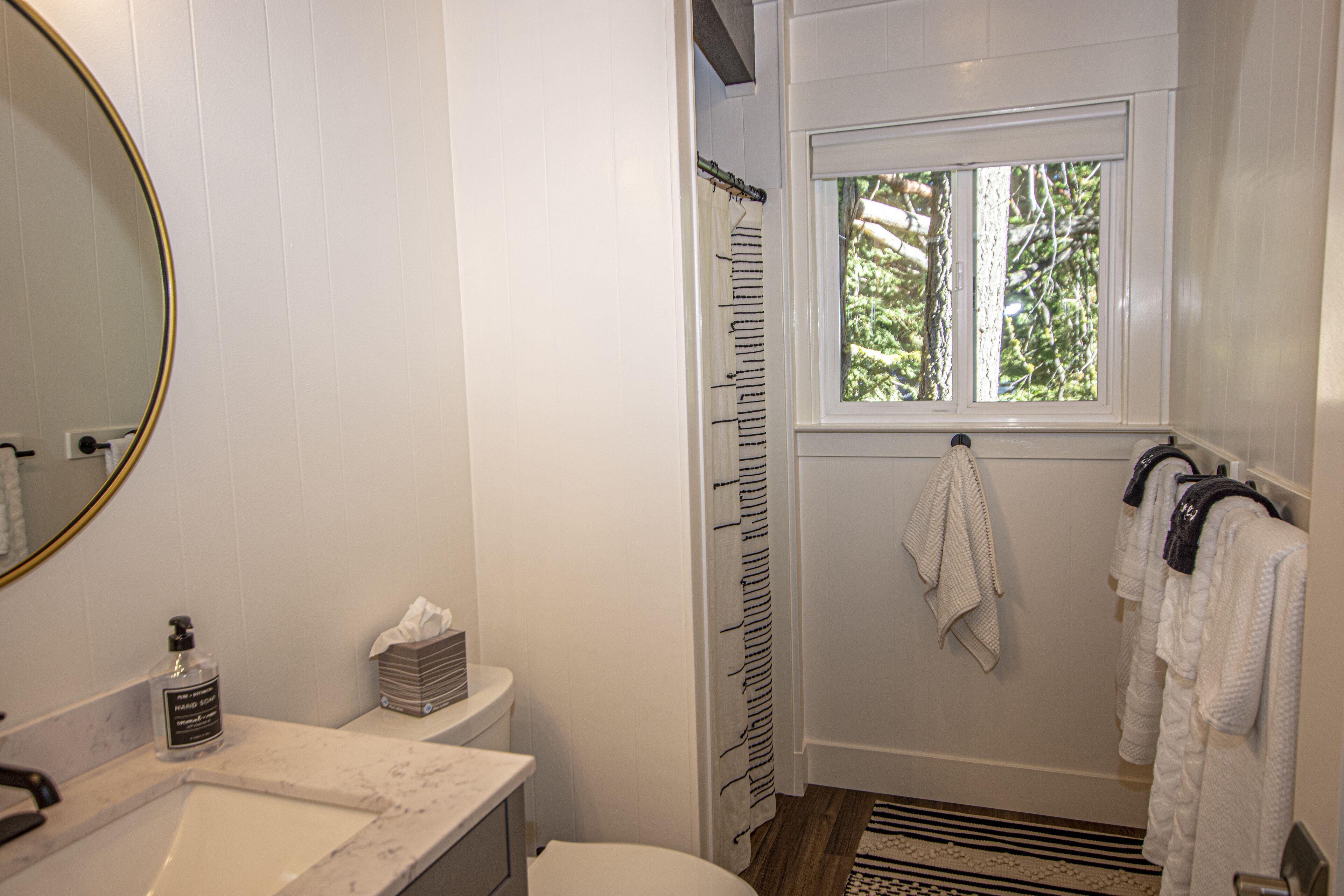 A bathroom with a white vanity, a mirror, a window, and a shower curtain.
