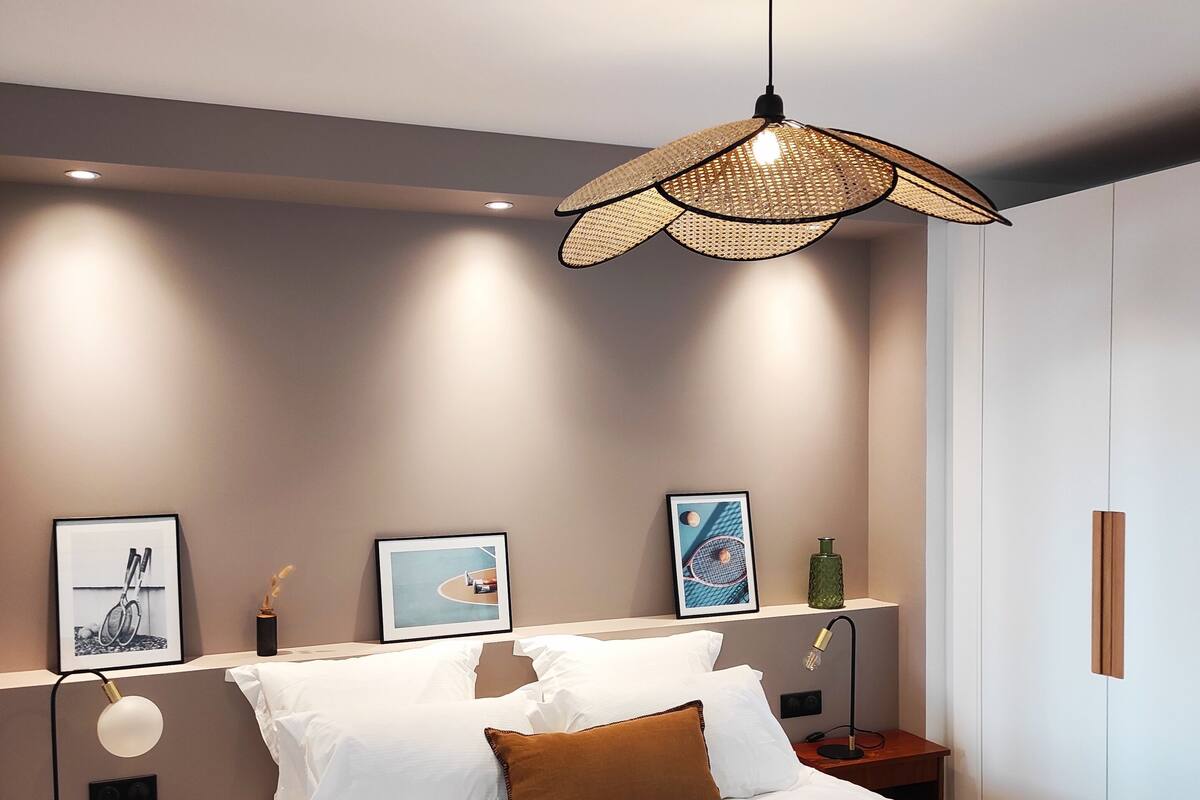 Een moderne slaapkamer met een groot bed, een hangende rotanlamp en kunstwerken in lijsten aan de muur.