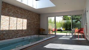 A modern indoor pool area with a skylight, a brick wall, and a patio with chairs. - Appart Hôtel & Spa La Villa Du Port (Vannes)