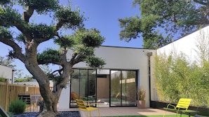 A modern outdoor patio with a large tree, yellow chairs, and a glass door leading to a pool area. - Appart Hôtel & Spa La Villa Du Port (Vannes)
