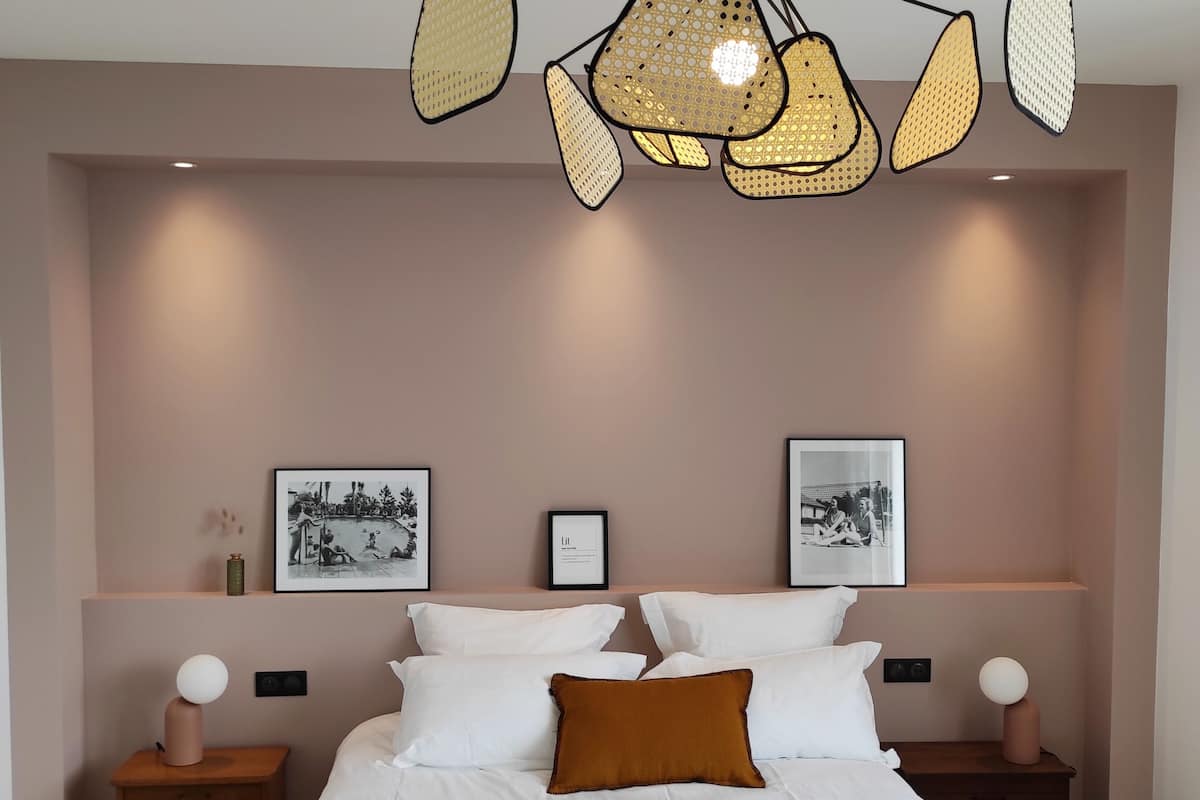 Een slaapkamer met een groot bed, twee nachtkastjes, een bijzondere hanglamp en afbeeldingen in lijsten aan de muur.